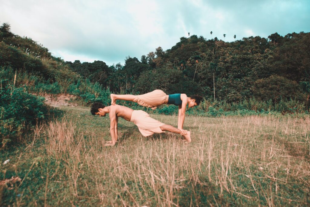 Woman balancing on man; both doing pushups in nature.